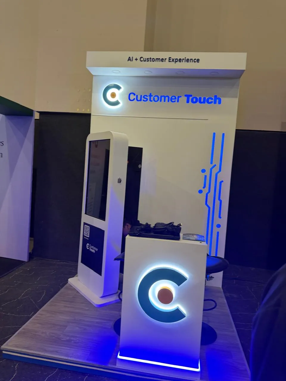 Stand de Customer Touch con el logo en forma de C iluminado y el rótulo «AI + Customer Experience».