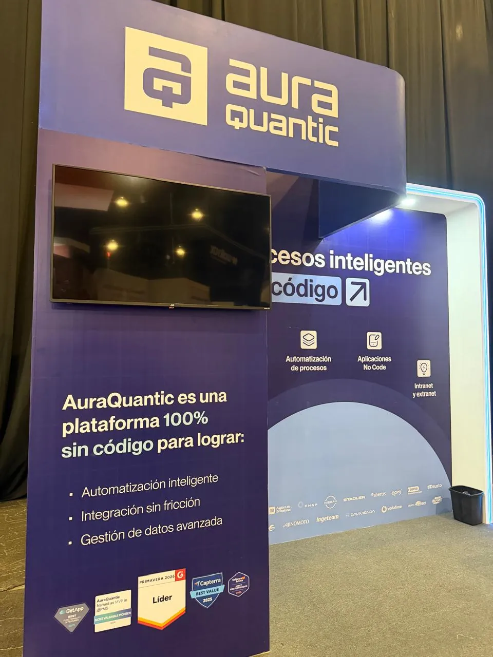 Stand morado de AuraQuantic con pantalla y el mensaje «Procesos inteligentes sin código», con varios sellos de reconocimiento.